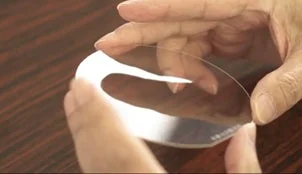 透明で薄く、湾曲した形状の物体を両手が優しく持っている様子