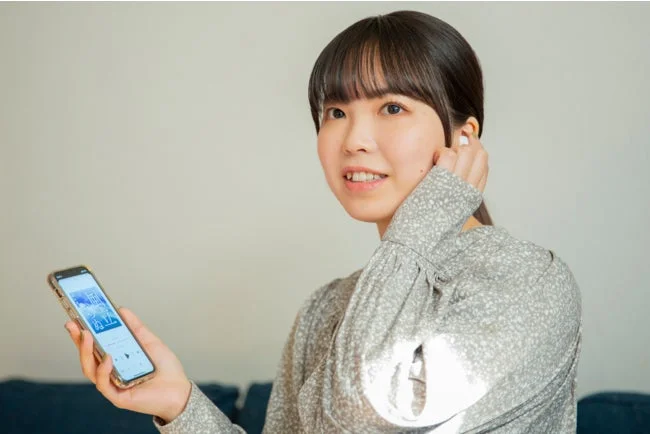 若い女性が屋内でスマートフォンを持ち、ワイヤレスイヤホンで音楽を聴いている様子