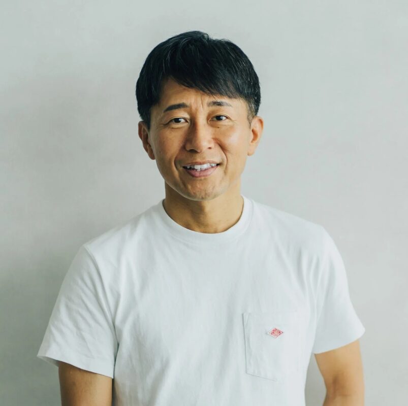 白いTシャツを着たアジア人男性がカメラに向かって微笑んでいるポートレート写真です。清潔感のあるシンプルな背景で、カジュアルな印象を与えます。