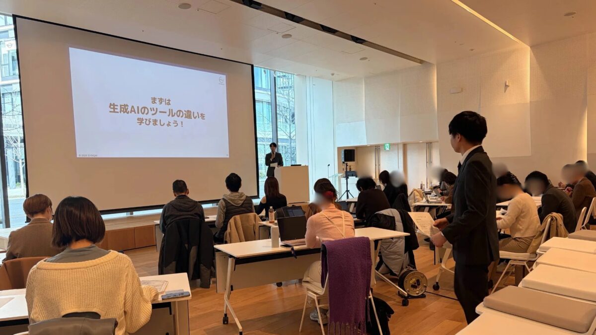 生成AIのツールに関するセミナーの様子を捉えた画像です。講演者が壇上で話しており、スクリーンには「まずは生成AIのツールの違いを学びましょう！」という文字が表示されています。多くの参加者が熱心に耳を傾けています。