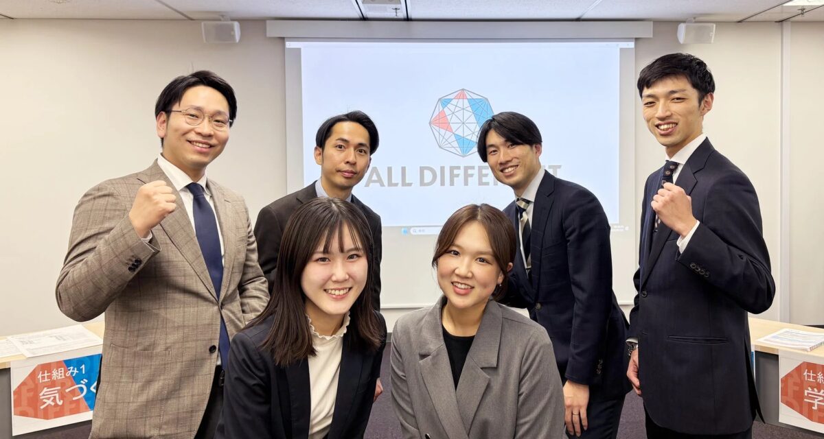 オフィスのような会議室で、ビジネスウェアを着た男女6人が笑顔でポーズをとっている集合写真です。背景のスクリーンには「ALL DIFFERENT」という文字とロゴが映し出されています。