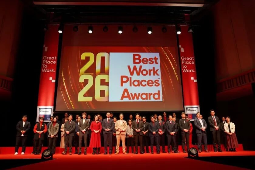 2026 Best Work Places™ Awardと書かれた大きなスクリーンを背景に、多くの人々がステージに立って記念撮影をしている様子です。