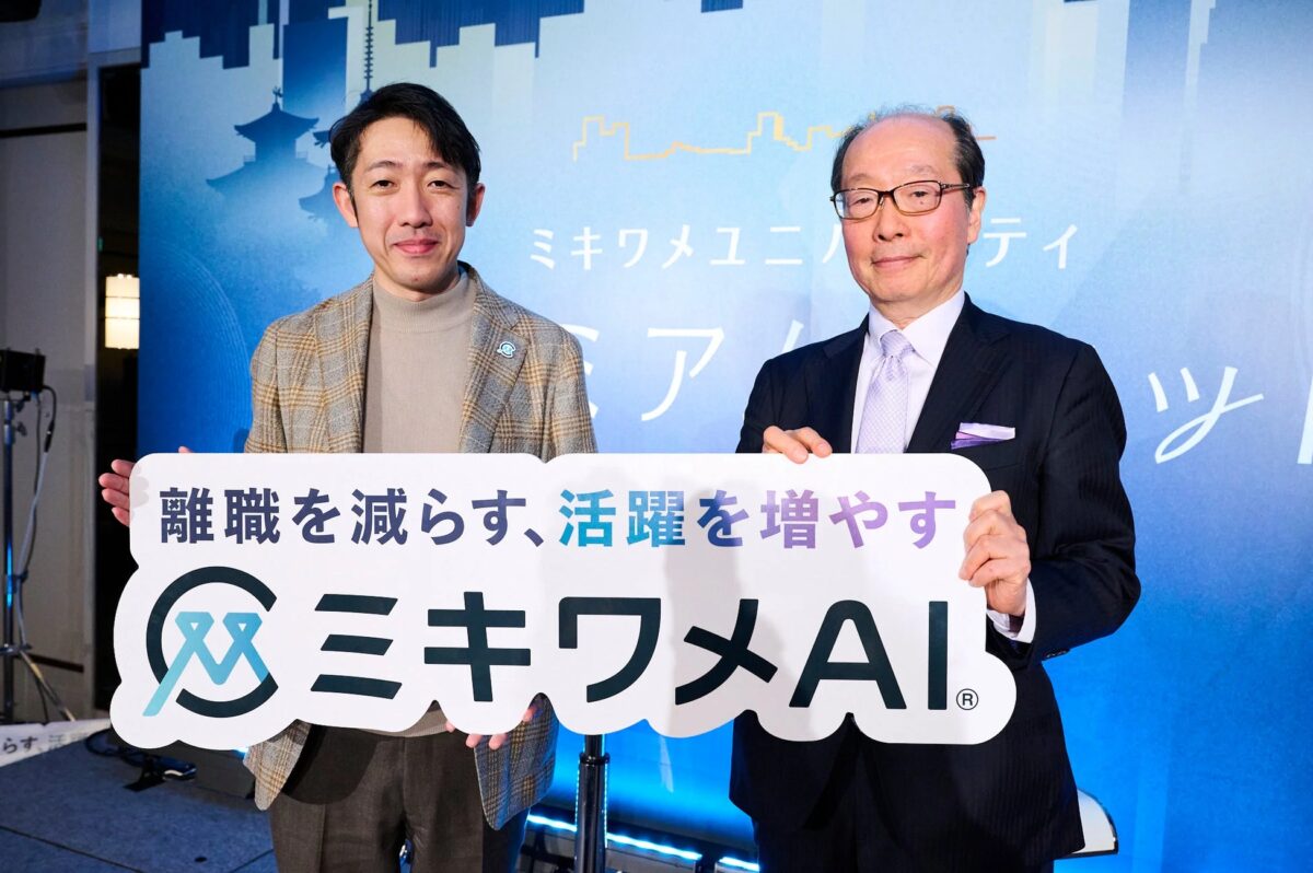 AIを活用した人事ソリューション「ミキワメAI」の発表イベントで、2人の男性が「離職を減らす、活躍を増やす」と書かれた看板を持って笑顔で立っている様子。背景には都市のシルエットが描かれ、ビジネスシーンでの利用が示唆されています。