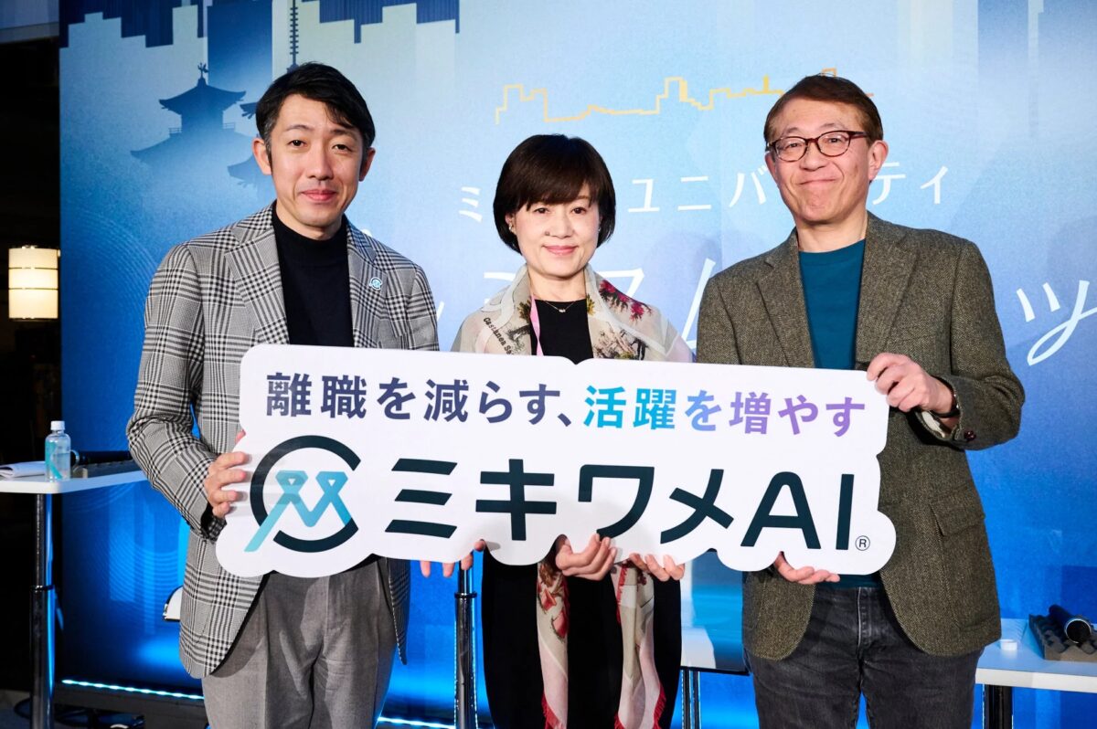 青い背景のステージで、2人の男性と1人の女性が「離職を減らす、活躍を増やす ミキワメAI」と書かれたボードを持って立っています。