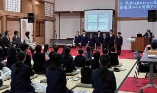 学生がステージで発表を行い、他の学生や大人が聴講している様子