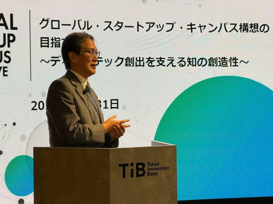 東京イノベーションベースのイベントで、スーツ姿の男性が「グローバル・スタートアップ・キャンパス構想」をテーマに講演中。