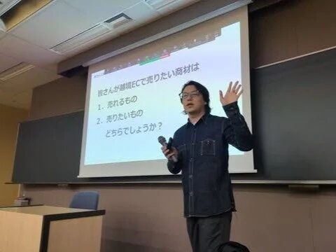 教室のような空間で、一人の男性がプロジェクタースクリーンを背景にプレゼンテーションを行っています。