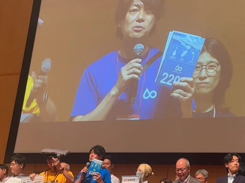 大きなスクリーンに映し出された男性がマイクを手に講演を行い、アクアポニクスに関する資料を見せている。