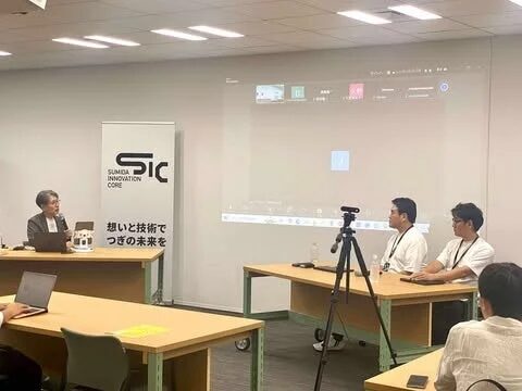 会議室でセミナーが開催されており、女性の講演者が登壇し、プロジェクターに資料が映し出されています。